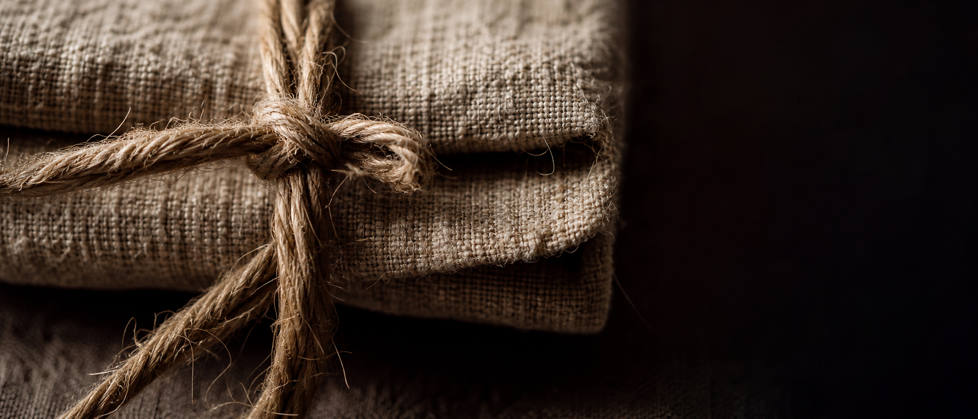 Extreme macro of hand-cut linen and knotted twine in a single raking candlelight, the weave sharp against deep shadow.
